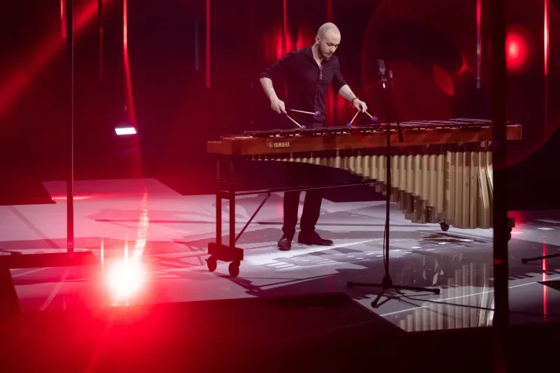 Glasbenik na rdeče osvetljenem odru igra na tolkalo marimba