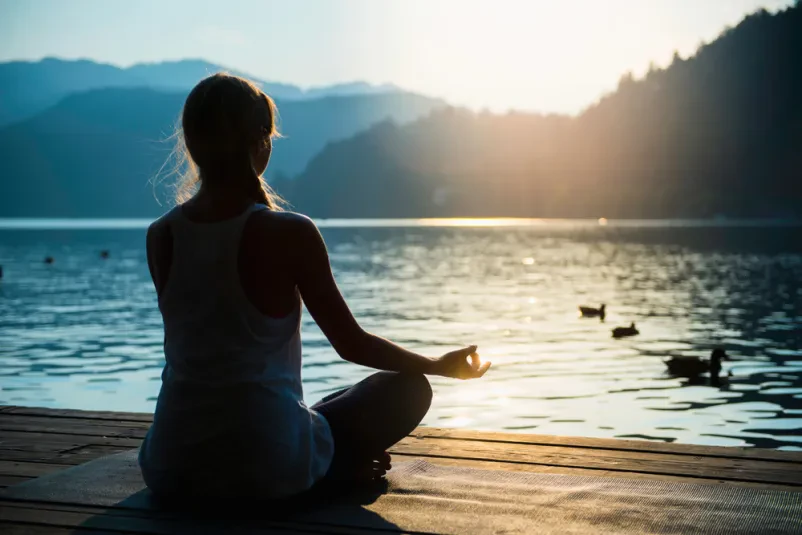 Vadba joge in meditacija na oddihu, ki poteka ob jezeru v naravi.
