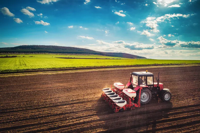 Dron posnetek prikazuje traktor, ki obdeluje veliko kmetijsko zemljišče. Takšna dela s traktorjem so ključna za pripravo tal v Mavčičah in okolici Kranja.