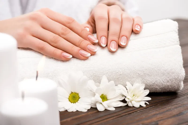 Sproščujoča nega rok in nohtov v salonu Bližnji posnetek ženske roke med sproščujočo spa nego, obkrožene z nežnimi rožami in dišečimi svečami za popolno manikuro in dobro počutje.