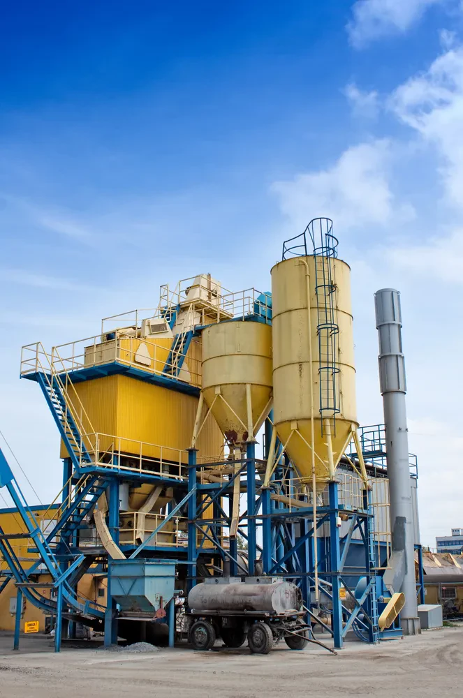 Industrijski kompleks tovarne cementa s poudarjenimi rumenimi silosi, ki se dvigajo proti nebu. Objekt je opremljen za pripravo različnih betonskih mešanic in izdelavo betona.