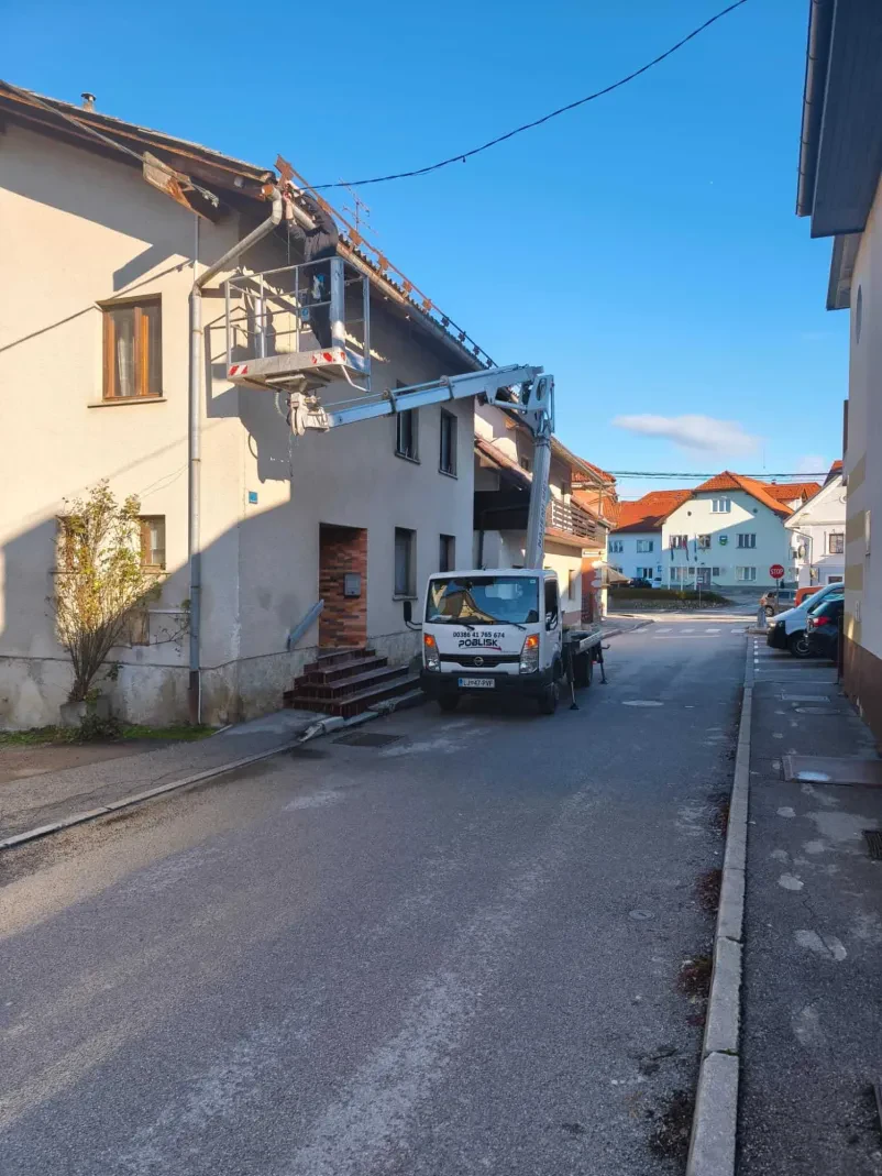 Delavec v oranžnem delovnem oblačilu popravlja cestno razsvetljavo z uporabo dvižne košare. Izposoja kvalitetnih delovnih strojev Osrednjeslovenska omogoča učinkovita dela na višini.