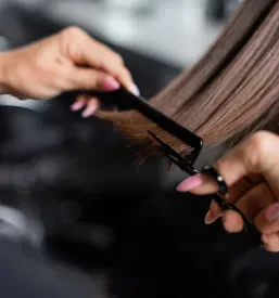 Bližnji posnetek profesionalnih frizerskih škarij in glavnika v rokah stilistke, ki natančno striže lase. Ključno za kakovosten Najboljši frizerski salon Ptuj.