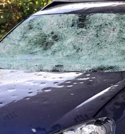 Avtomobil z močno poškodovano karoserijo in razbitim vetrobranskim steklom po ekstremnem neurju s točo. Takšne obsežne poškodbe zahtevajo strokovno popravilo udrtin po toči Dolenjska in pogosto tudi zamenjavo delov.