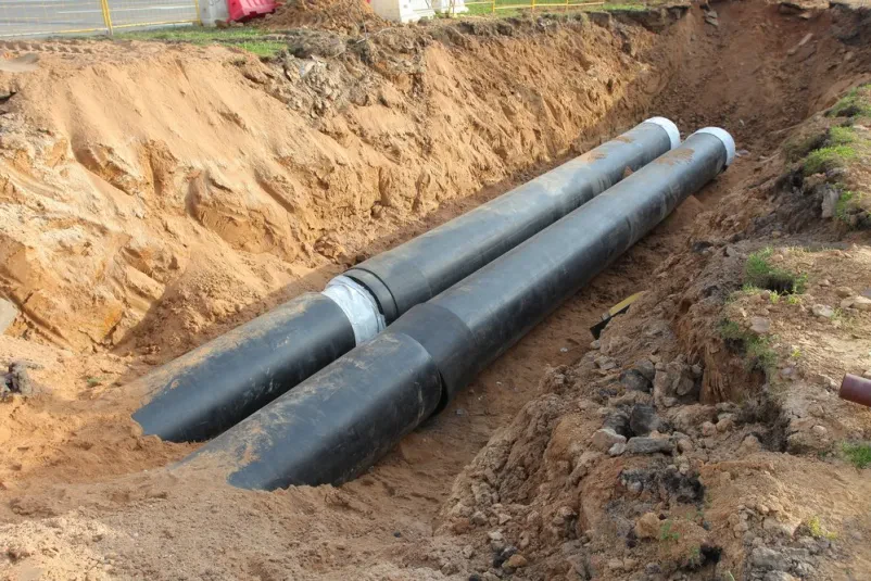 Novo položene vodovodne cevi ležijo v izkopanem jarku, pripravljene za vgradnjo v tla, kar je ključen del infrastrukturnih del.