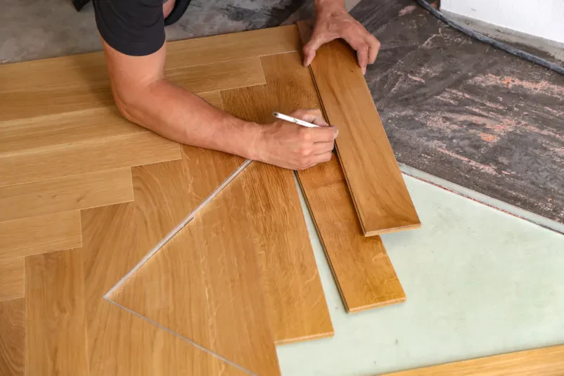 Delavec previdno namešča leseno laminatno ploščo na tla, s poudarkom na natančnosti in pravilni postavitvi.