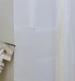 Delavec natančno nanaša omet na steno. Takšna zaključna gradbena dela v Celju in Ljubljani so ključna za brezhibno prenovo.