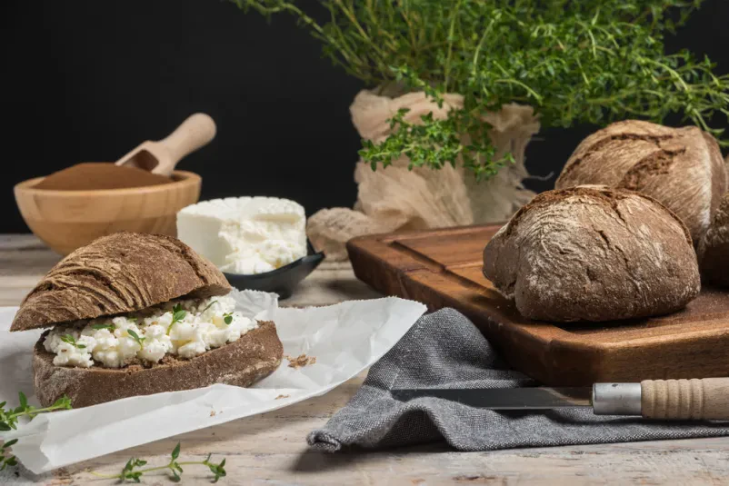 Sveže pečen domač kruh s kremasto skuto in aromatičnim timijanom, pripravljen po tradicionalni kmečki recepturi.