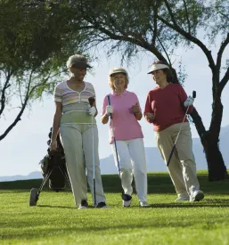 Tri aktivne ženske v zrelih letih se skupaj sprehajajo po zelenem igrišču za golf in uživajo v naravi ter prijetnem druženju.