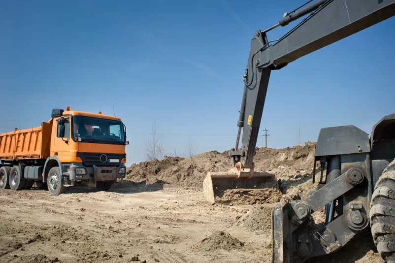 Hidravlični bager in tovornjak na gradbišču Učinkovit hidravlični bager natovarja zemljo na kiper tovornjak, kar ponazarja profesionalne gradbene izkope in kiper prevoze Posavje.