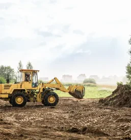 Močan rumeni čelni nakladalnik skrbno poravnava teren in pripravlja zemljišče za gradnjo novega objekta, kar je del zemeljskih izkopov.