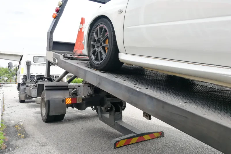 Modri avtomobil se s pomočjo kljuke in verige naklada na ploščad avtovleke, pripravljen za prevoz varno in učinkovito.