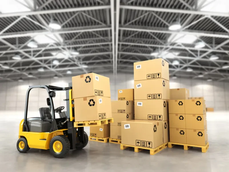 Viličar premika kartonske škatle na paletah v modernem skladišču, kar prikazuje učinkovito logistiko in dostavo paletne robe.