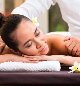 Sproščena indonezijska ženska leži na masažni mizi v spa centru. Prejema wellness masažo z eteričnimi olji, ki prinašajo globoko sprostitev.
