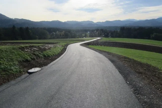 Rekonstrukcija lokalne ceste Širok posnetek rekonstrukcije ceste Ribič - Dovže, ki prikazuje sveže asfaltirano površino, pomembno za lokalno infrastrukturo.