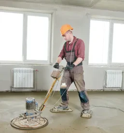 Gradbeni delavec vodi električni stroj za glajenje med postopkom mokrega brušenja betonskih tal, s čimer doseže visokokakovostno površino, idealno za Kvaliteteno brušenje betona Goriška.