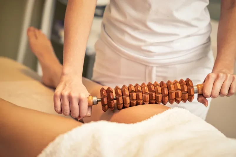 Terapevtka izvaja anticelulitno maderoterapijo na ženski nogi v spa salonu. Kvalitetna maderoterapija v Novem mestu izboljšuje prekrvavitev in gladi kožo.