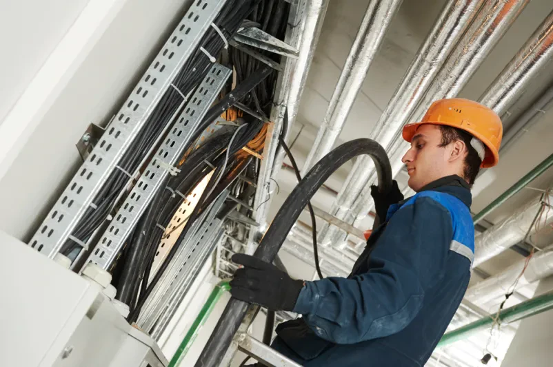Električar namešča kable v omarico z varovalkami Električar s ključem natančno pritrjuje industrijski kabel v razdelilno omarico, kar zagotavlja pravilno in varno delovanje.