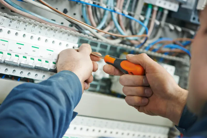 Bližnji posnetek rok električarja, ki s izvijačem zateguje stikalno opremo v varovalki, kar je ključnega pomena za zanesljivo delovanje.