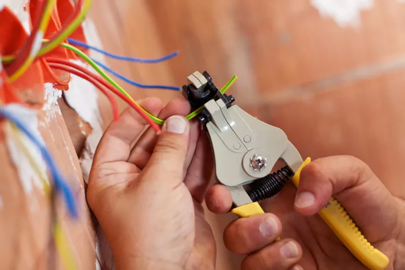 Bližnji posnetek rok električarja, ki s kleščami skrbno lušči izolacijo z žic, pripravlja jih za varno in pravilno priključitev.