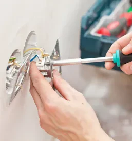 Bližnji posnetek rok električarja, ki namešča novo električno vtičnico v steno, pazi na detajle za varno in funkcionalno uporabo.