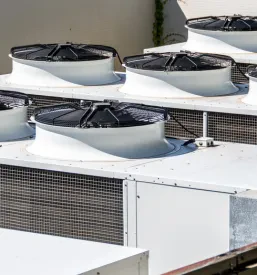 Več industrijskih klimatskih enot, nameščenih na strehi komercialne stavbe. Poudarjajo moderno tehnologijo HVAC.