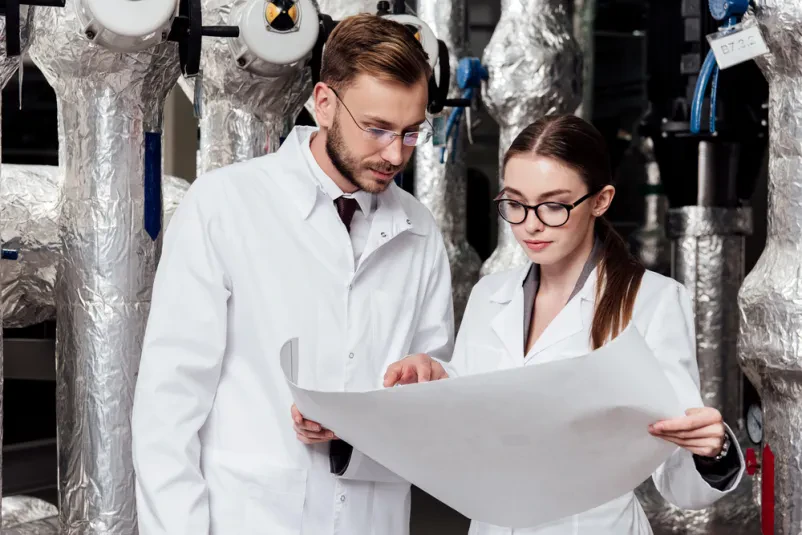 Dva inženirja v očalih se osredotočata na podroben načrt, ki prikazuje zasnovo industrijskega sistema kompresorjev, kar je ključnega pomena za kvalitetno konstruiranje industrijskih strojev v podjetjih v Goriški regiji.