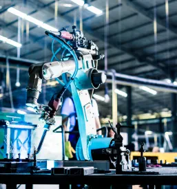 Napreden varilni robot v industrijski hali zagotavlja visoko natančnost in učinkovitost pri proizvodnji kovinskih izdelkov.