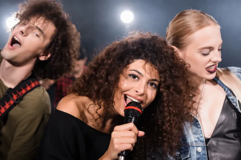Veseli vokalist rock skupine med energičnim nastopom Nasmejan vokalist rock skupine poje v mikrofon na odru. Osvetljen je z reflektorji, kar ustvarja dinamično vzdušje med nastopom.