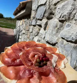 Visokokakovosten pršut v naravni obliki, obešen v sušilnici, poudarja pristno domačo hrano in kulinariko.