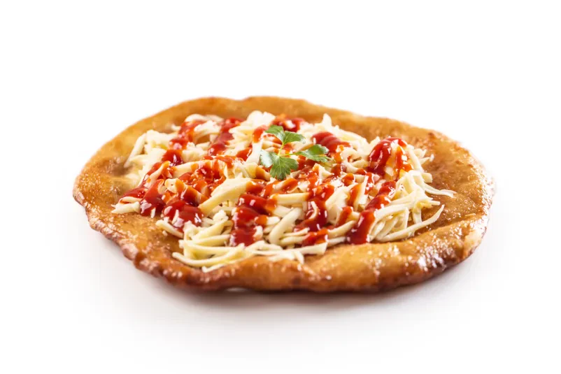 Okusen madžarski langoš s sirom in ketchupom Sveže pripravljen madžarski langoš, posut z naribanim sirom in prelit s ketchupom ter česnom, postrežen na leseni podlagi.