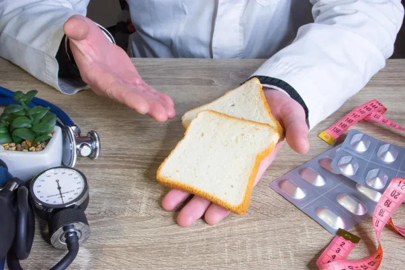Zdravnik nutricionist med posvetom drži v roki in kaže pacientu kos kruha, pojasnjuje prehranske koristi in pomen v jedilniku.