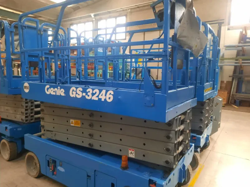 Robusta škarjasta dvižna ploščad Genie GS 3246 s 12-metrsko višino v prostrani skladiščni hali, pripravljena na delo.