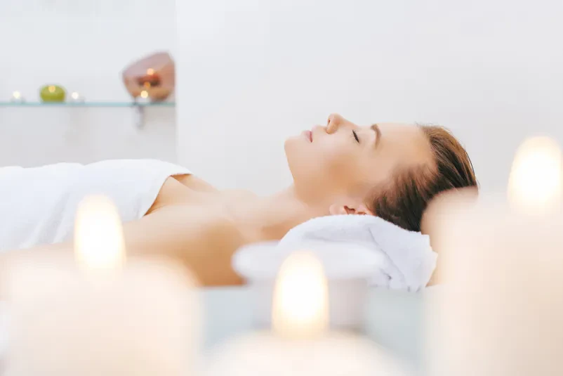 Ženska mirno leži na masažni mizi v spa salonu, popolnoma sproščena in pripravljena na razvajanje. Uživajte v tišini in udobju.