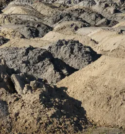 Urejene kupe izkopane zemlje in peska na gradbišču, pripravljene za nadaljnje urejanje terena in pripravo temeljev.