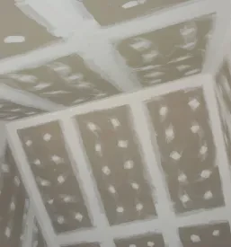 Pogled na že nameščen suhomontažni strop iz mavčnih plošč na gradbišču, ki čaka na zaključno obdelavo, kar je tipičen rezultat suhomontažnih sistemov v Šmartnem ob Paki.