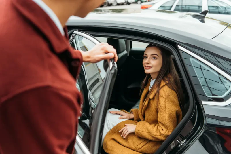 Voznik taksija odpira vrata potnici Ustrežljiv taksist odpira vrata avtomobila nasmejani potnici. Zanesljiv in ugoden taxi Primorska zagotavlja prijetno izkušnjo.