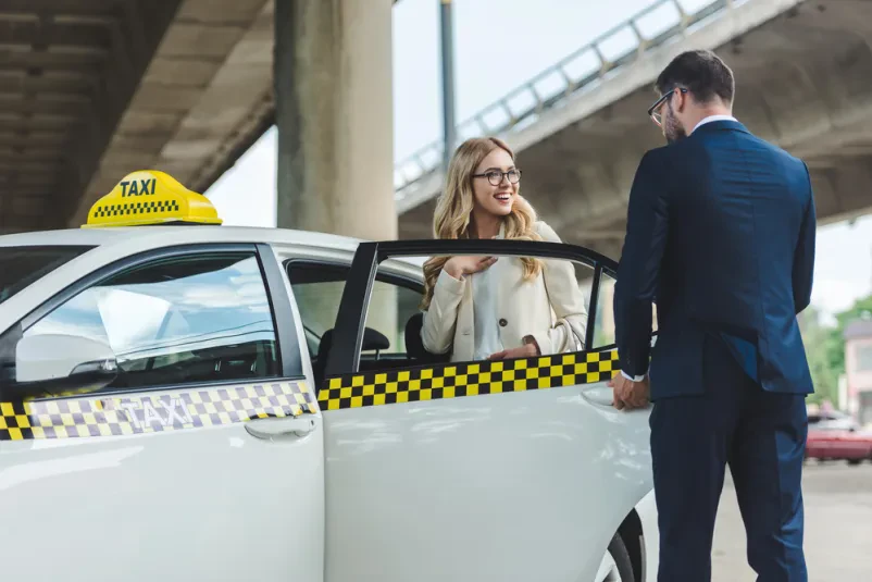 Gospod odpira vrata taksija nasmejani ženski Urejen gospod odpira vrata taksija nasmejani blondinki, ki že udobno sedi v vozilu, pripravljena na prijeten prevoz po mestu.