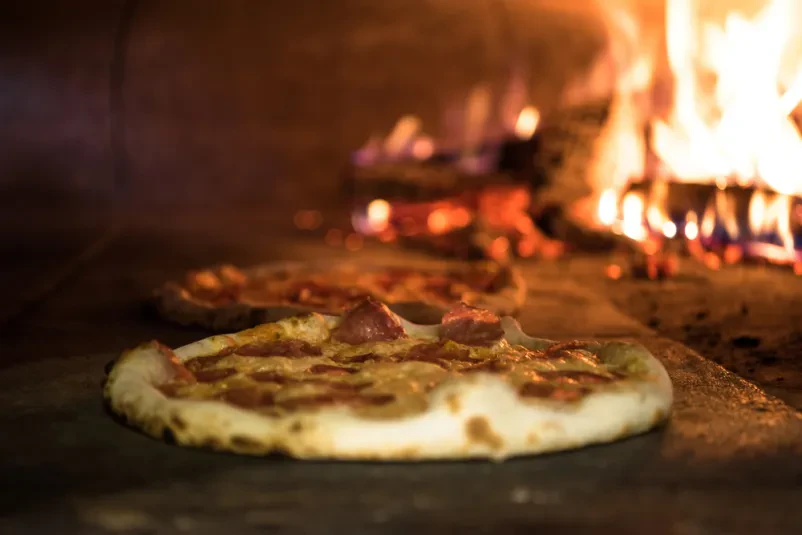 Pica se peče v krušni peči Približan pogled na okusno italijansko pico, ki se peče v tradicionalni krušni peči, z živahnimi plameni v ozadju, kar zagotavlja hrustljavo skorjo.