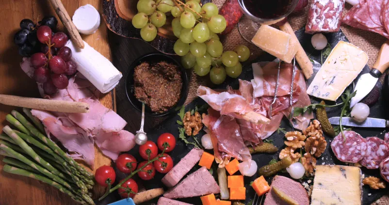 Raznolika plošča suhih mesnin in sira Plošča z izbiro suhih mesnin, vključno s tanko narezano šunko, salamo in pašteto, dopolnjena z različnimi siri, pripravljena za postrežbo.