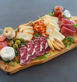 Živahna in pisana plošča tapas jedi, ki vključuje pester izbor domačih suhomesnatih izdelkov Črnomelj, dimljenih mesnin, sirov, orehov in sveže rukole.