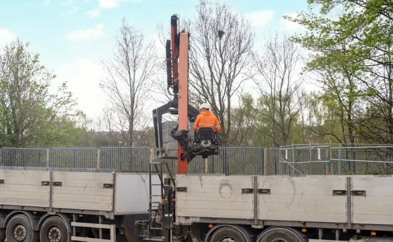 Detajl HIAB dvigala z oprijemom Približni posnetek delujočega HIAB dvigala, ki s posebnim prijemalom natančno dviguje in postavlja opeke na gradbišču, kar prikazuje preciznost dvigovanja tovora.