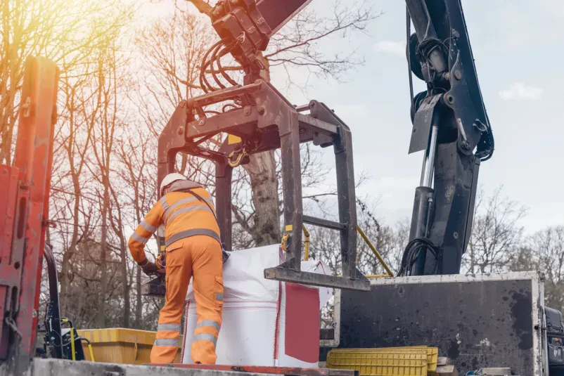 HIAB tovornjak dostavlja opeke na gradbišče Velik tovornjak s HIAB dvigalom in priključkom za opeke raztovarja gradbeni material na sončnem gradbišču. Zanesljivi HIAB prevozi Logatec zagotavljajo učinkovito logistiko.