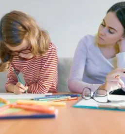Mlada učiteljica pomaga deklici pri pisanju v zvezek. Zasebna ura je odlična za individualno učenje Ljubljana in hiter napredek pri inštrukcijah.