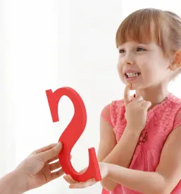 Majhna deklica sedi v logopedovi pisarni in aktivno sodeluje pri vaji izgovorjave. Pomoč je ključna za govorni in jezikovni razvoj.