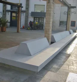 Masivna in moderna betonska klop v javnem parku ponuja udoben in vzdržljiv prostor za počitek med zelenjem.