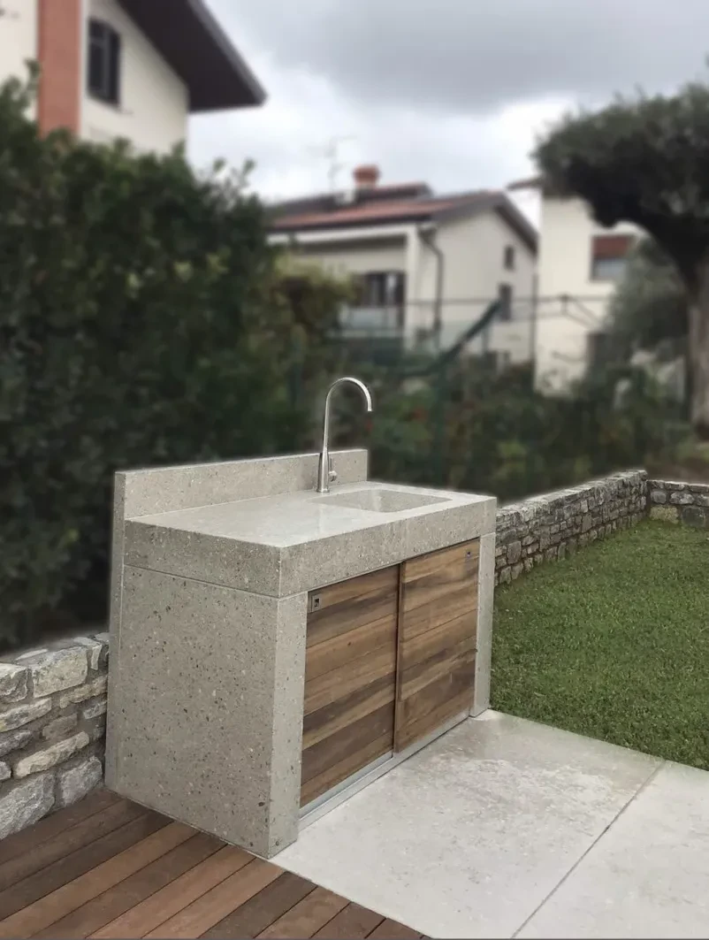 Prikaz moderne zunanje kuhinje z betonskimi pulti, vgrajenim umivalnikom in funkcionalnim prostorom za delo.