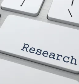 Približan posnetek računalniške tipkovnice z jasno poudarjeno tipko 'RESEARCH'. Simbolizira intenzivno iskanje in zbiranje podatkov.
