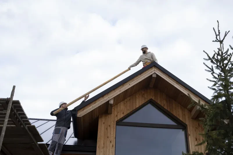 Ekipa krovcev med montažo strehe Skupina izkušenih krovcev v zaščitni opremi skrbno postavlja streho, s čimer izvajamo krovska, kleparska dela Medvode na terenu.