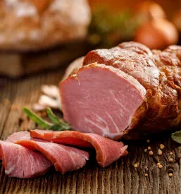 Narezano dimljeno meso je postreženo na rustikalni leseni mizi, okrašeno s svežimi zelišči in začimbami.